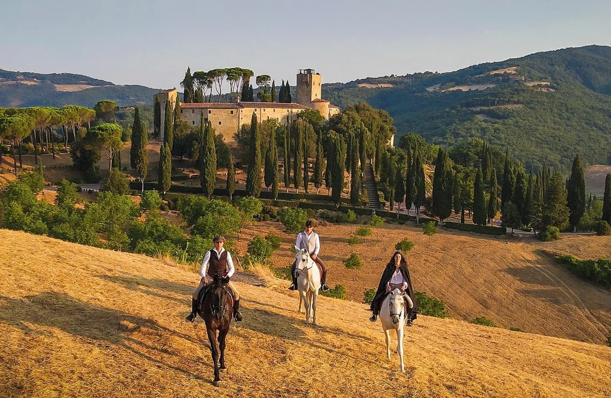 Riders on horseback in front of a hilltop estate in the Italian countryside